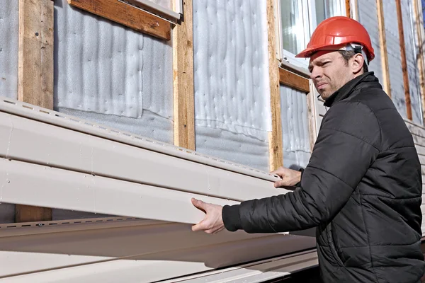 Een werknemer installeert panelen beige siding op de gevel Rechtenvrije Stockafbeeldingen