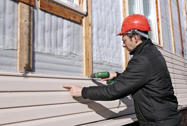 A worker installs panels beige siding on the facade clipart