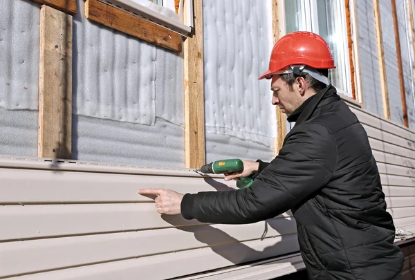 Een werknemer installeert panelen beige siding op de gevel Stockfoto