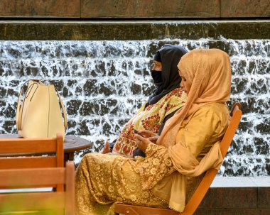 Londra, Birleşik Krallık - 30 Mayıs 2021: Geleneksel giysili iki bayan Cabot Meydanı 'ndan çekilen bir şelalenin önünde oturdu