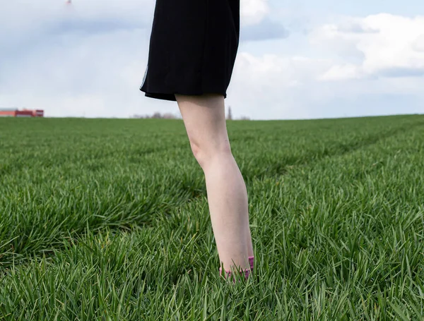 White girl legs in black skirt on green field