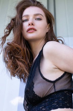 Pencerenin önünde siyah kıvırcık saçlı bir mankenin portresi.