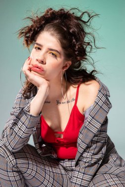 Beyaz Avrupalı manken kırmızı elbiseli, elleri yeşil yüzün yanında oturuyor.