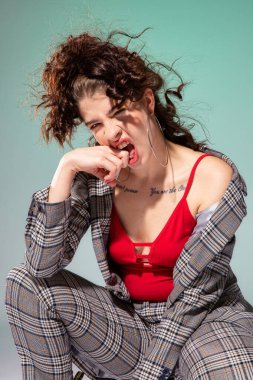 Beyaz Avrupalı manken kırmızı elbiseli, elleri yeşil yüzün yanında oturuyor.