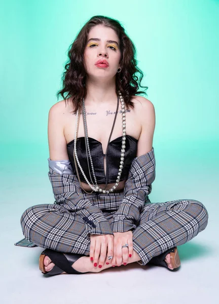 Beyaz kıvırcık saçlı kadın yeşil üzerinde tek başına oturuyor.