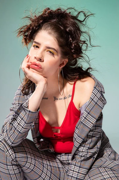 Beyaz Avrupalı manken kırmızı elbiseli, elleri yeşil yüzün yanında oturuyor.