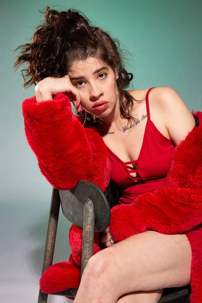 Kırmızı elbiseli Avrupalı beyaz kadın yeşil üzerinde tek başına oturuyor.