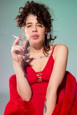 Kırmızılı sigara içen beyaz kız mankeni yeşilde izole edilmiş.