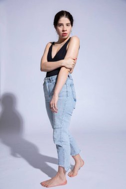 Açık mavi kotlu, ciddi bir beyaz kız. Gri üzerinde izole edilmiş.