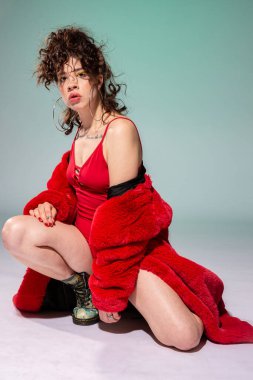 Kırmızı elbiseli beyaz kız yeşilde tek başına oturuyor.