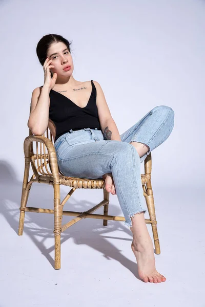 Girl in jeans sits in chair isolated on grey