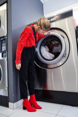 Çamaşır makinesiyle oturan genç beyaz kadın.