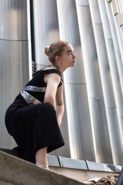 Siyah giysili beyaz kadın. Metal paneller arkasında.