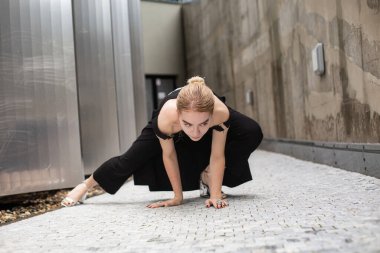 Siyah elbiseli beyaz kadın şehir yolunda taş döşemede oturuyor.