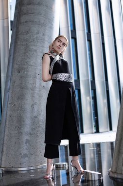 Siyah elbiseli, şehir binasının arka planında duran beyaz model kız.