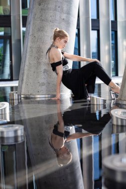 Genç beyaz model kız, şehir binası geçmişiyle yerde oturuyor.