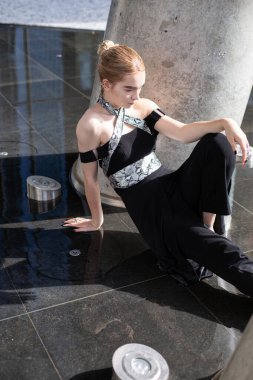 Sarışın, beyaz model kız dışarıda yerde oturuyor.