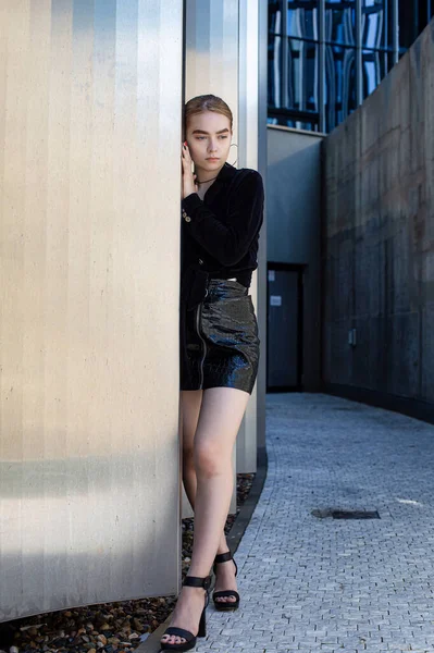 Şehir şeridinde siyah elbiseli genç kız duvara dokunuyor.