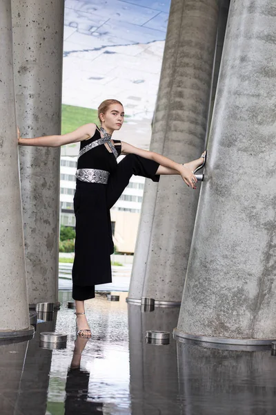 Siyah kokteyl elbisesi içindeki beton sütunların arasında Avrupalı genç bir kız.