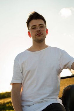 Dışarıda sarı saçlı genç beyaz bir adam arabaya dokunuyor.