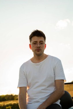 Dışarıda sarı saçlı, kaputun yanında sigara içen genç, beyaz bir adam.