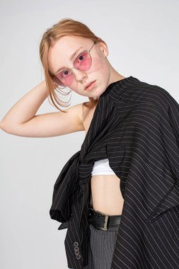 Güneş gözlüklü ve ceketli genç bir kadın saçlarına dokunuyor.