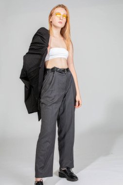 Spor ceketli genç bir kadın stüdyoda duruyor.