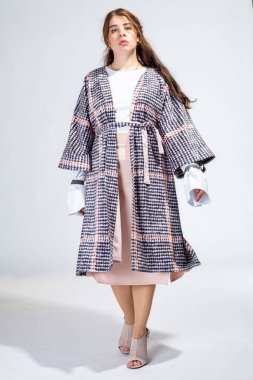 Dolgun dudaklı genç beyaz kadın açık gri üzerinde tek başına duruyor.