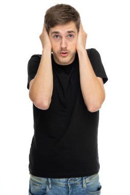 Genç yakışıklı, uzun boylu, zayıf, kahverengi saçlı, kulaklarını siyah gömlekle kaplayan beyaz arka planda izole edilmiş kot pantolonlu adam.