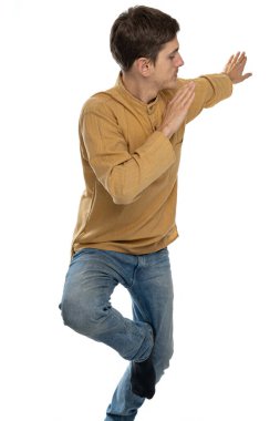 Genç yakışıklı, uzun boylu, zayıf, kahverengi saçlı Tai Chi pozu veren, beyaz arka planda izole edilmiş mavi kotlu, koyu renk gömlekli beyaz bir adam.