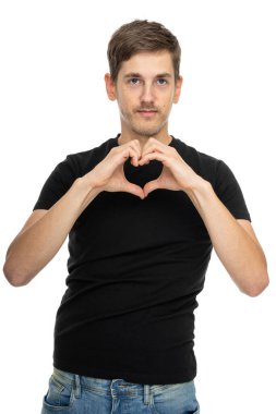 Genç, uzun boylu, zayıf, kahverengi saçlı, siyah gömlekli, beyaz arka planda izole edilmiş kot pantolonlu, kalp hareketi yapan bir adam.