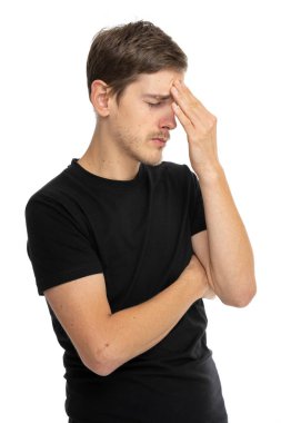 Genç yakışıklı, uzun boylu, zayıf, kahverengi saçlı, başı ağrıyan beyaz adam beyaz arka planda siyah gömleğiyle alnına dokunuyor.