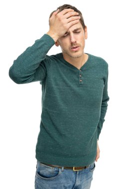 Genç, uzun boylu, zayıf, kahverengi saçlı, baş ağrısı olan, koyu yeşil kazaklı, beyaz arka planda izole edilmiş kot pantolonlu bir adam.