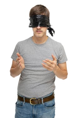 Genç, uzun boylu, zayıf, kahverengi saçlı, siyah plastik çantalı, beyaz arka planda, gözlerini gri gömlekle kapayan beyaz bir adam.