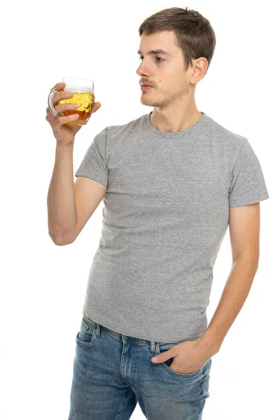 若いですハンサムな背の高いスリム白い男で茶色の髪でグレーシャツで青ジーンズでビールのガラスと分離白の背景 — ストック写真