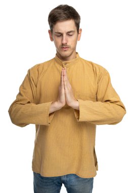 Genç yakışıklı, uzun boylu, zayıf, kahverengi saçlı beyaz adam beyaz arka planda koyu renk gömlekle dua ediyor.