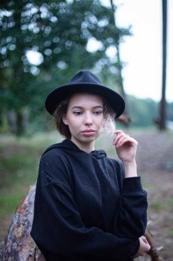 Siyah elbiseli, arkasında orman olan beyaz bir kadın.