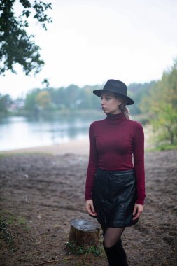 Siyah şapkalı, arkasında göl olan beyaz bir kadın.