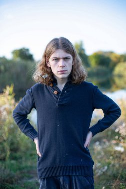 Uzun saçlı beyaz Avrupalı genç adam gölün arkasında duruyor.