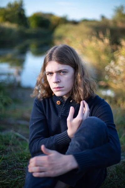 Серьезный Молодой Европейский Мужчина Длинными Волосами Озером Позади — стоковое фото