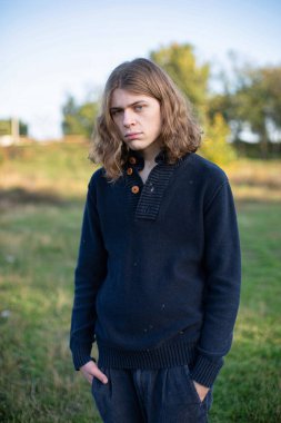 Üzgün, beyaz Avrupalı, yeşil çimlerin üzerinde duran sarı saçlı genç adam.