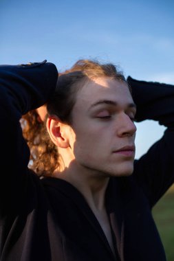 Genç Avrupalı beyaz adam, uzun saçlı, gün batımının arkasında gökyüzü olan.