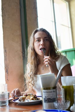 Koyu saçlı Avrupalı bir kız kafenin arkasında pencereyle yemek yiyor.