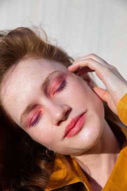 Duvarın yanında parlak makyajlı genç bir kız portresi.