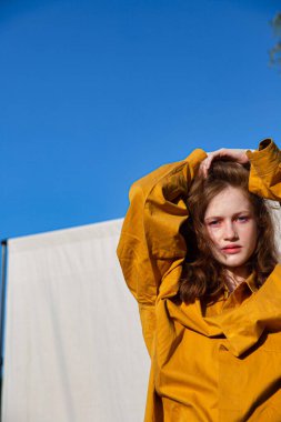 Parlak makyajlı beyaz kız, açık mavi gökyüzü arkasında.