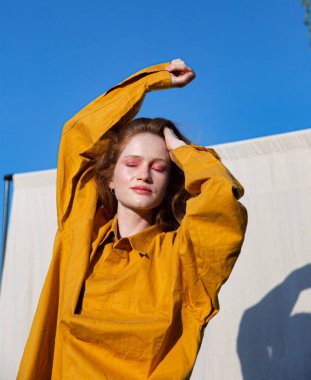 Arkasında açık mavi gökyüzü olan parlak makyajlı genç beyaz kız.