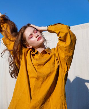 Siyah saçlı, sarı elbiseli, gözleri kapalı ve arkasında mavi gökyüzü olan beyaz Avrupalı bir kız.