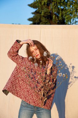 Parlak makyajlı, kızıl saçlı, elinde çiçekler olan bir kız.