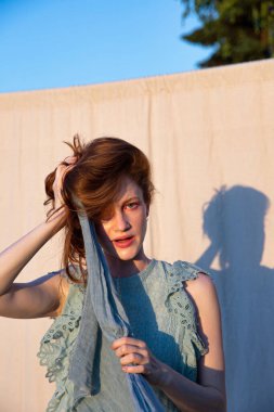 Parlak makyajlı Avrupalı genç bir kadın kızıl saçlarını tutuyor.