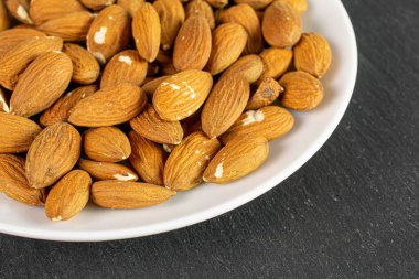 Beyaz seramik tabakta bir sürü badem var.